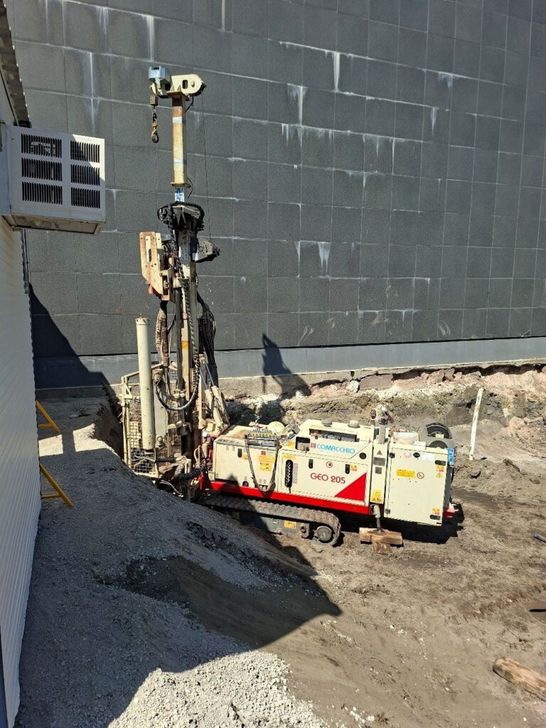 Comacchio GEO205 drilling rig set up on a gravel pad beside a building