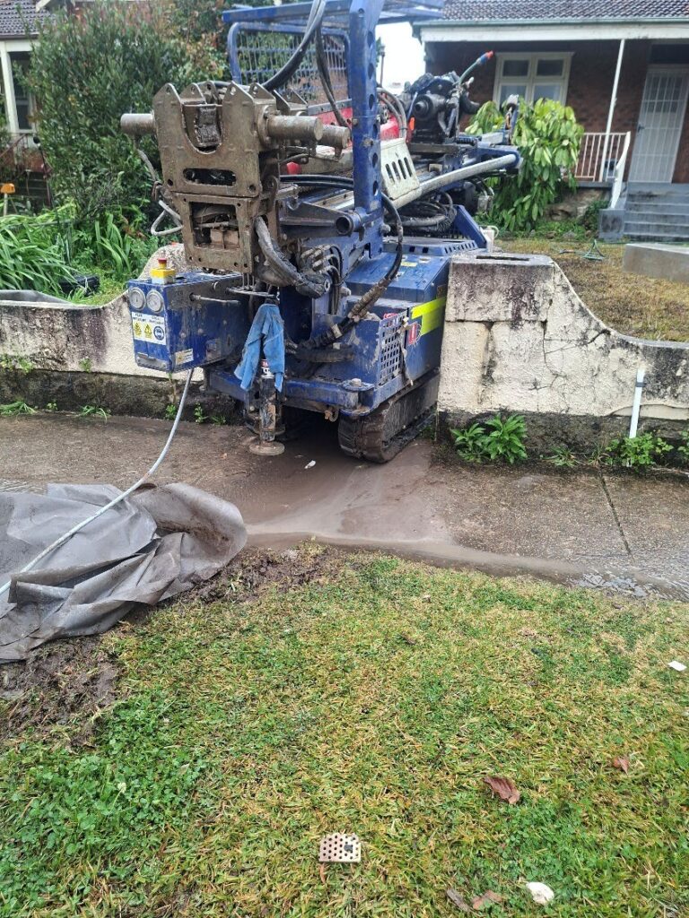 Christie CE108 drilling rig working on grass beside a retaining wall